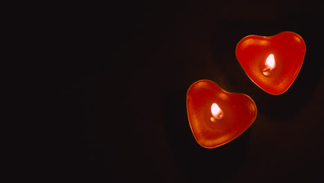 Close-Up-Of-Two-Romantic-Lit-Heart-Shaped-Red-Candles-On-Black-Background-With-Copy-Space